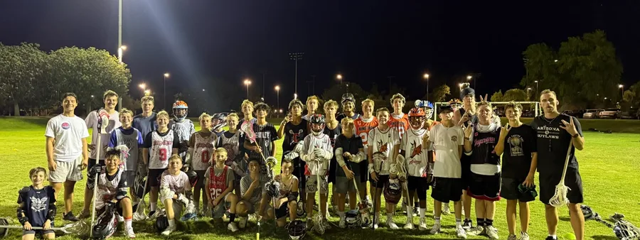 Valley Boys Lacrosse athletes and coaches posing together under the field lights